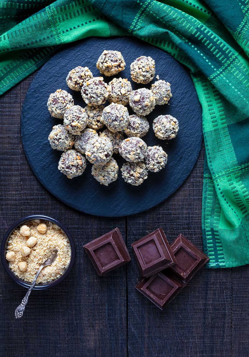 Hazelnut Truffles on a large plate, green tablecloth chocolate squares and finely chopped roasted hazelnuts on its side