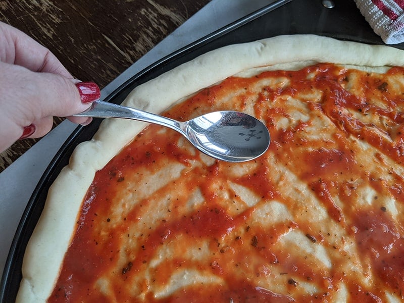simple pizza dough in a pizza pan with pizza sauce spread on top using a spoon