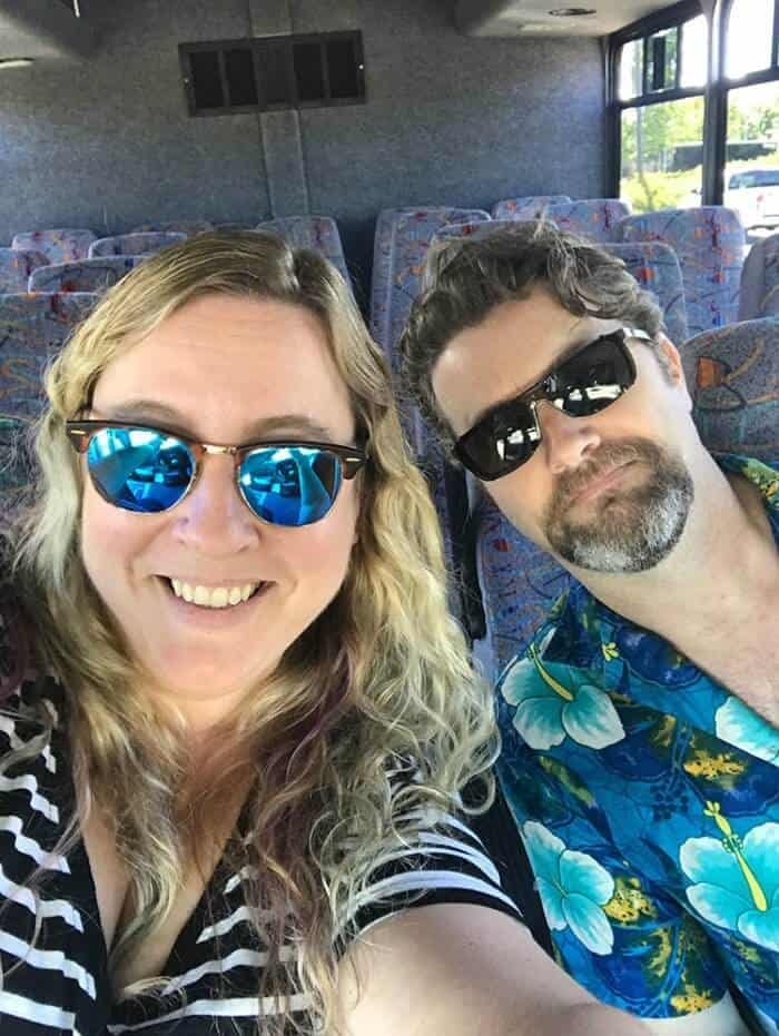 Selfie on shuttle going to the pier, woman wearing stripe black blouse and man wearing blue floral polo shirt