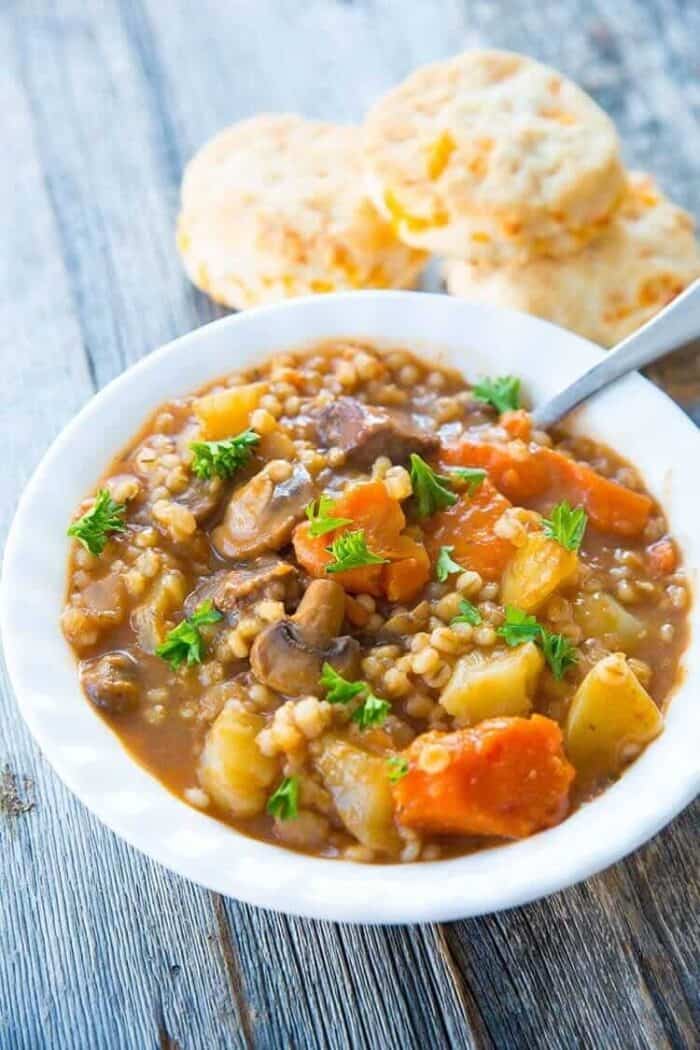 delicious beef and barley stew in a white soup bowl, garnish with fresh parsley leaves