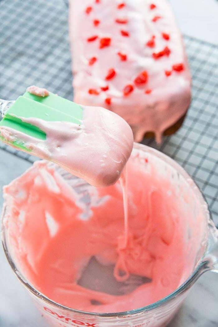 Close up Cherry Icing Glaze in a Pyrex measuring cup with green spatula