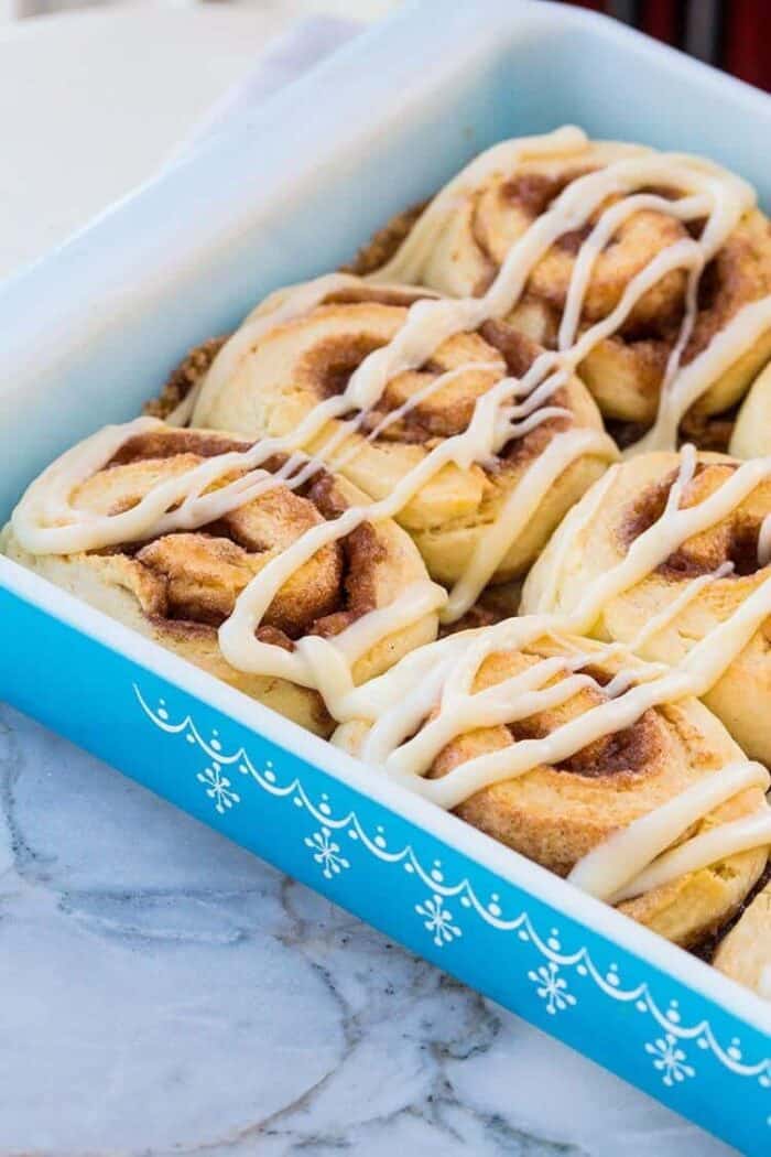 Close up of Fluffy No Rise Cinnamon Rolls with Glaze in a Blue Pyrex Baking Pan on marble background