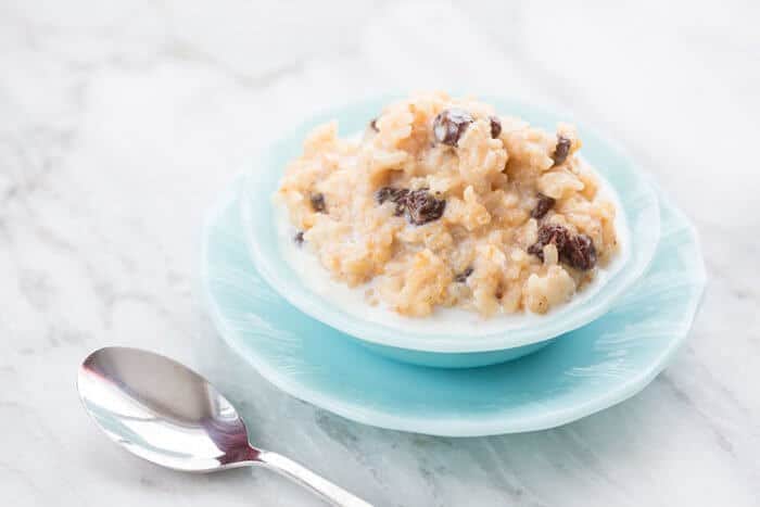 Instant Pot Rice Pudding in a Jade blue bowl over jade blue plate on marble background, a spoon beside it