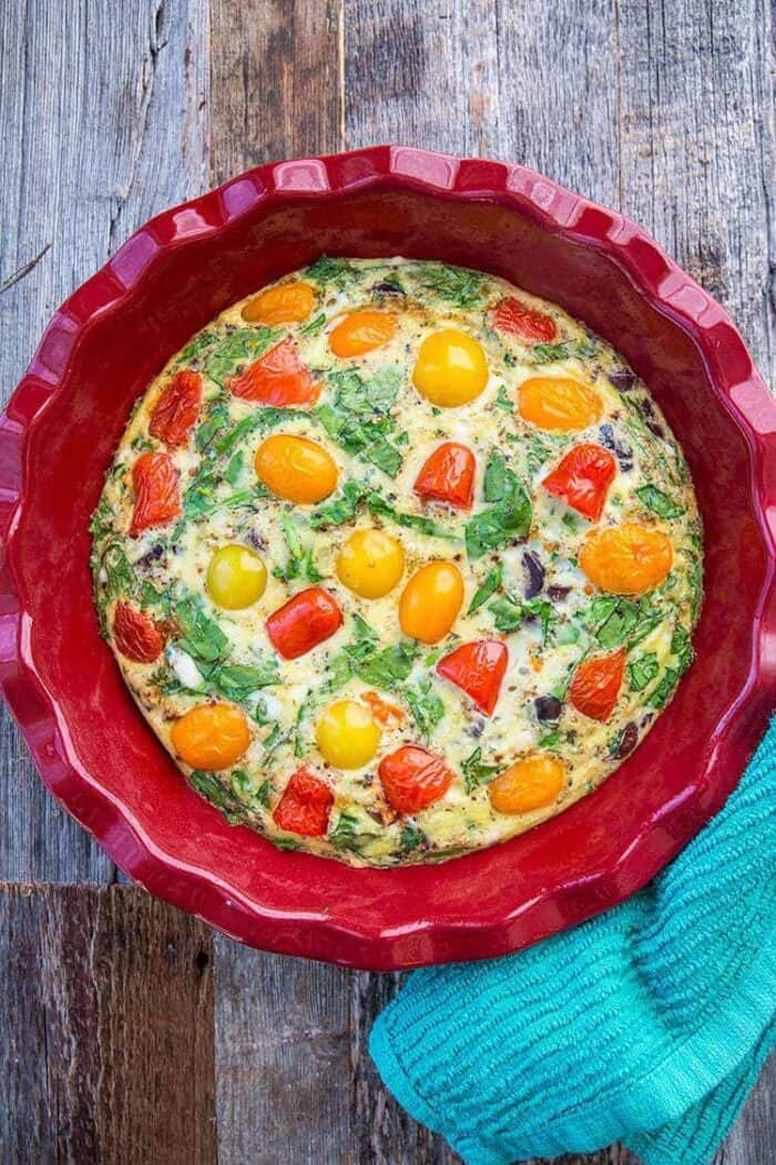 Mediterranean Vegetable Frittata in Large Red Bowl with cherry tomatoes, chopped kalamata olives and crumpled feta