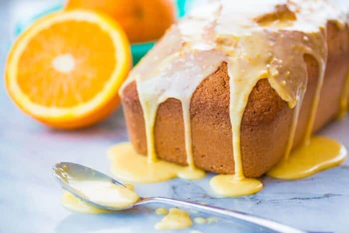 Amazing Orange Loaf Cake Topped with Orange Icing Glaze, Sliced Orange on Background