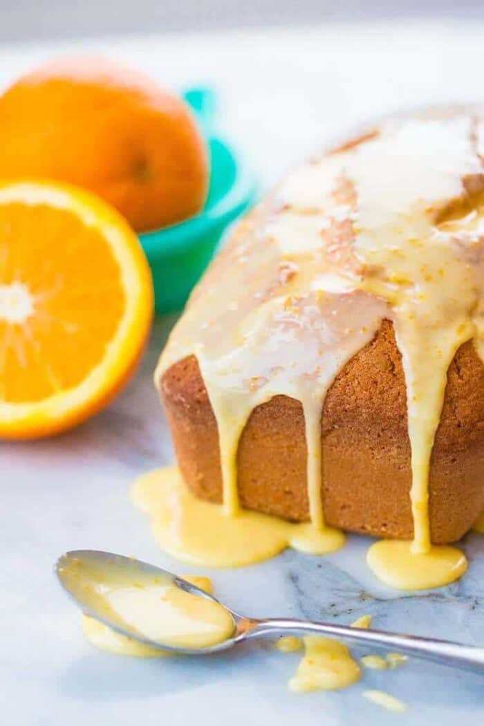 Close up Orange Loaf Cake Topped with Orange Icing Glaze, Sliced Orange on Background