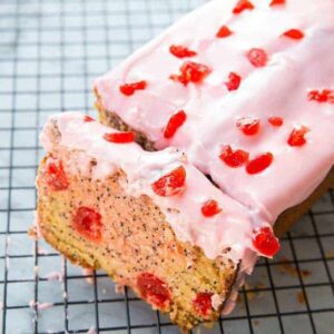sliced cherry poppy seed loaf cake with glaze on wire baking rack