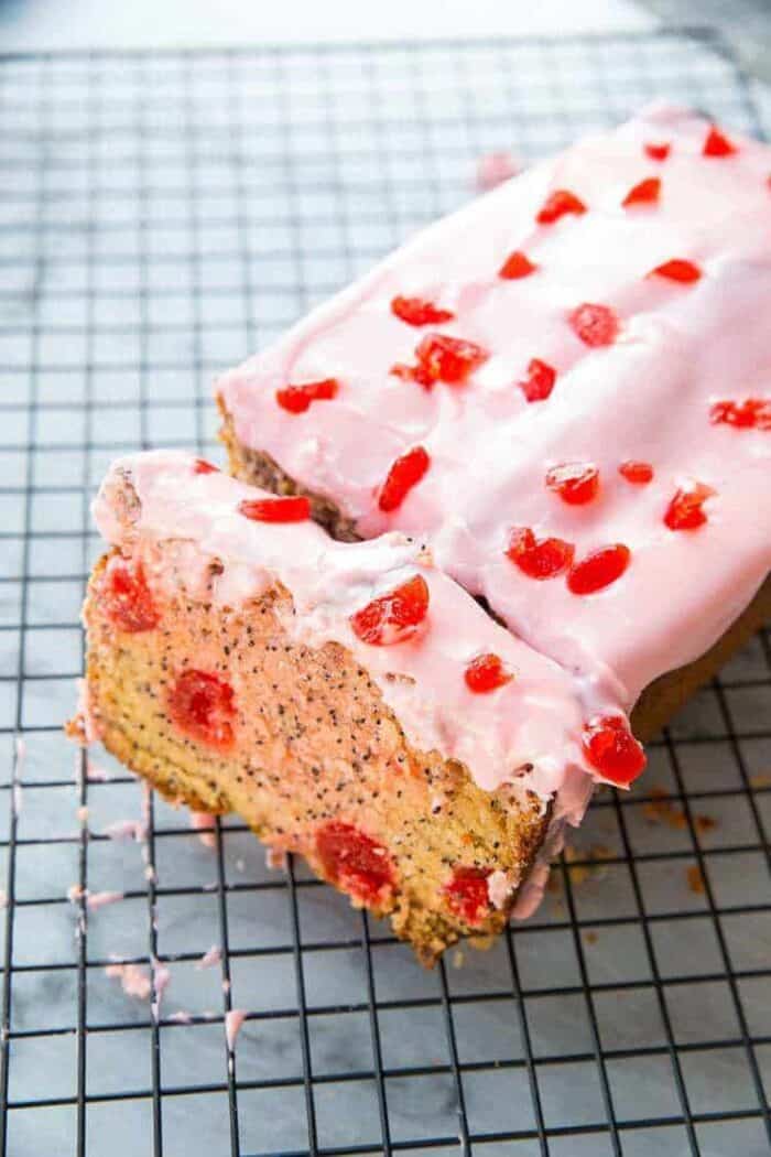 sliced cherry poppy seed loaf cake with glaze on wire baking rack