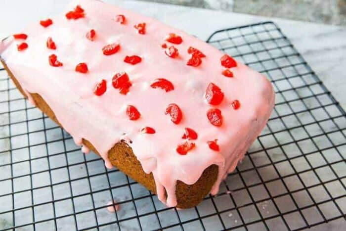 Cherry Poppy Seed Loaf Cake with cherry icing glaze on black cooling rack