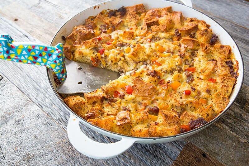 white casserole dish with pie server in between the cuts in Sausage & Peppers Overnight Breakfast Strata