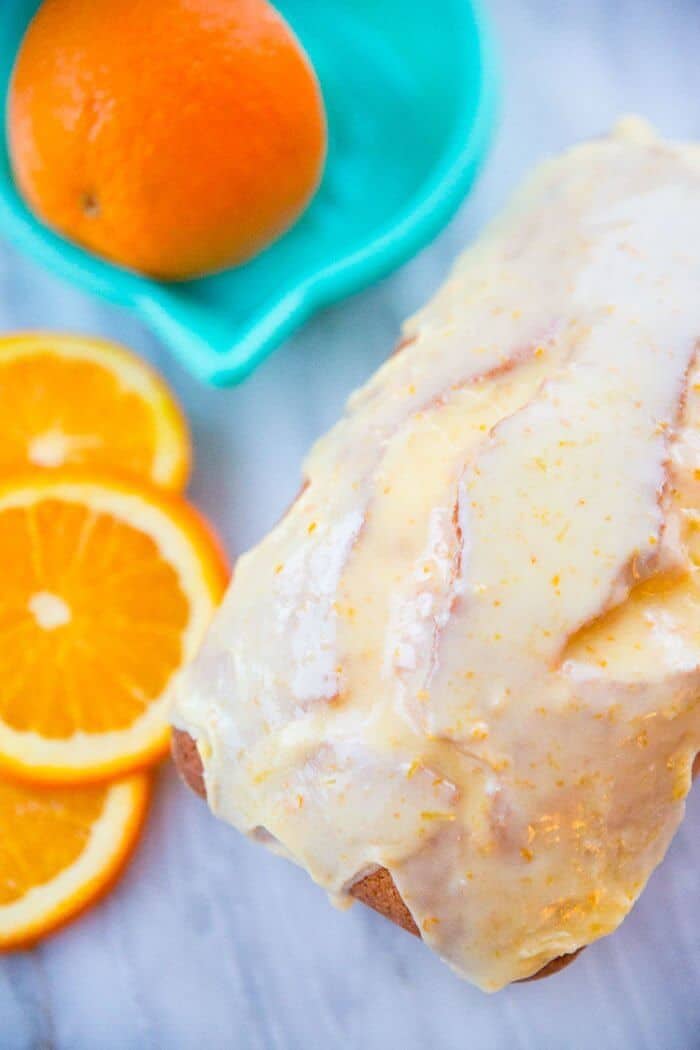 Close up of Orange Icing Glaze on top of Loaf cake, orange slices on background