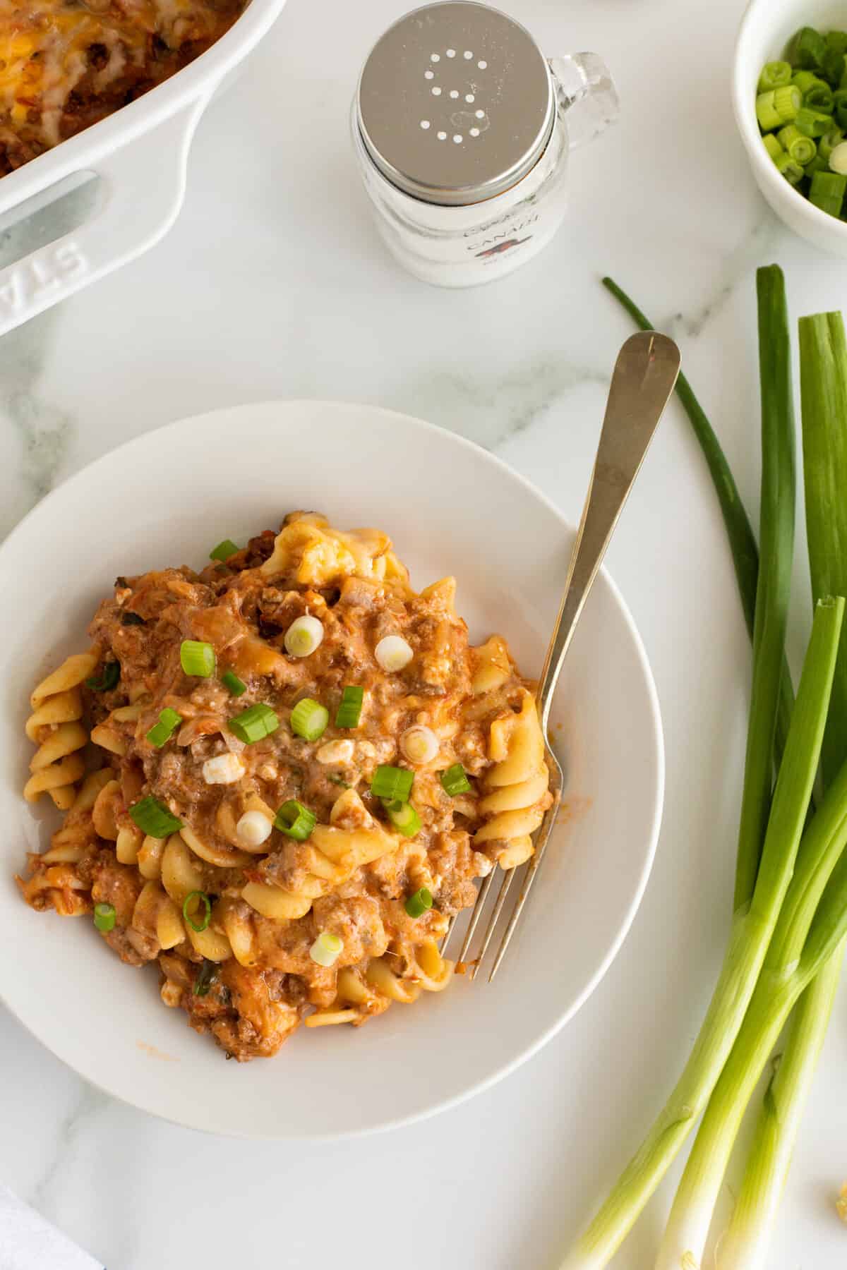 sour cream noodle bake on a white plate with a fork and whole green onions beside the plate