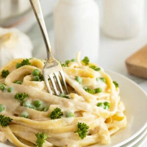 5 ingredient cream cheese Alfredo sauce piled high on a white plate with a fork in the top.