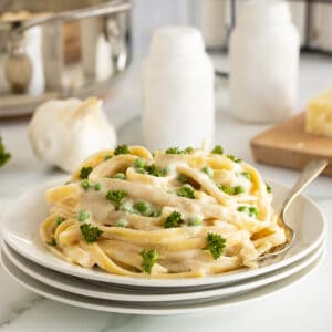 5 ingredient cream cheese Alfredo sauce piled on a stack of white plates