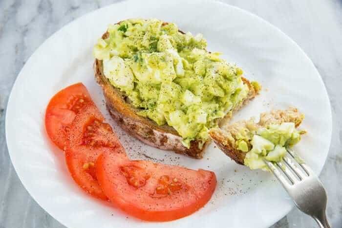 white plate with slices of red tomatoes and open faced toasted bread topped with Avocado Egg Salad