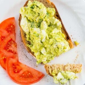 white plate with slices of red tomatoes and open faced toasted bread topped with Avocado Egg Salad