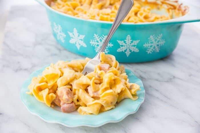 Creamy Ham & Noodle Casserole in a small ruffled turquoise plate and in turquoise casserole dish