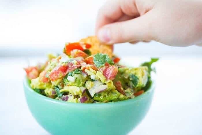 hand dipping chips into guacamole in a blue bowl