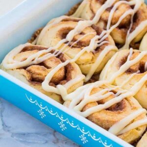 Close up of Fluffy No Rise Cinnamon Rolls with Glaze in a Blue Pyrex Baking Pan on marble background