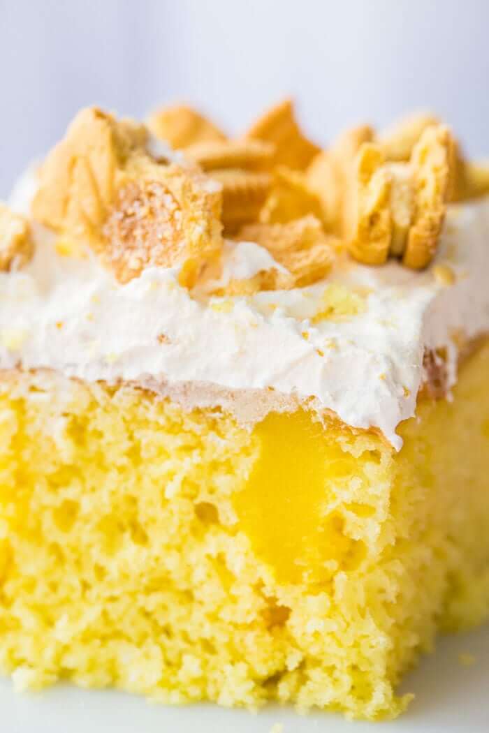 Close up Slice of Lemon Better Than Sex Cake Topped with Whipped Cream and Crushed Lemon Cookies in Ruffle Plate