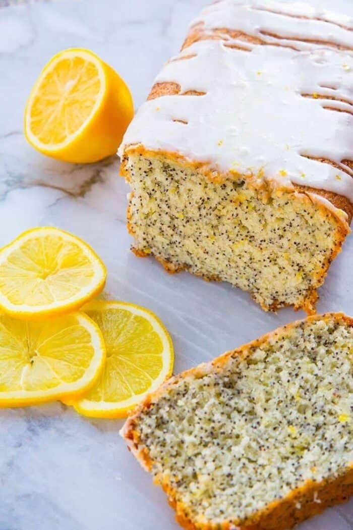 Lemon Poppy Seed Loaf Cake with Lemon Icing Glaze with lemons on a white marble surface