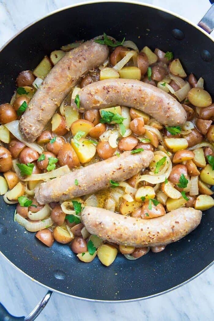 Top down shot of Sweet Mustard Sausage and Potato Skillet with parsley in a large black skillet