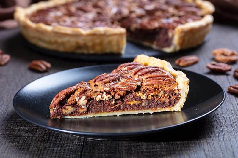 a slice of Chocolate Pecan Pie on a black medium serving plate and the remaining part of the pie on its background