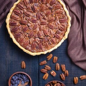 brown polka dot tablecloth on dark wood background, whole Chocolate Pecan Pie with a cup of whole pecan and a cup of chocolate chips beside it