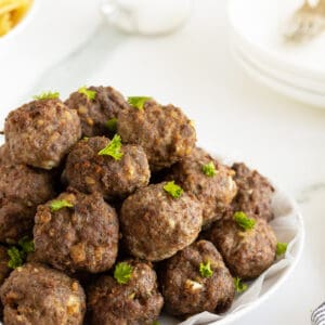 homemade meatballs piled high on a large white plate garnished with parlsey