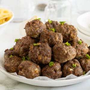 homemade meatballs piled high on a large white plate garnished with parsley