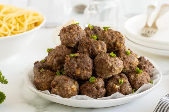 homemade meatballs piled high on a large white plate garnished with parsley