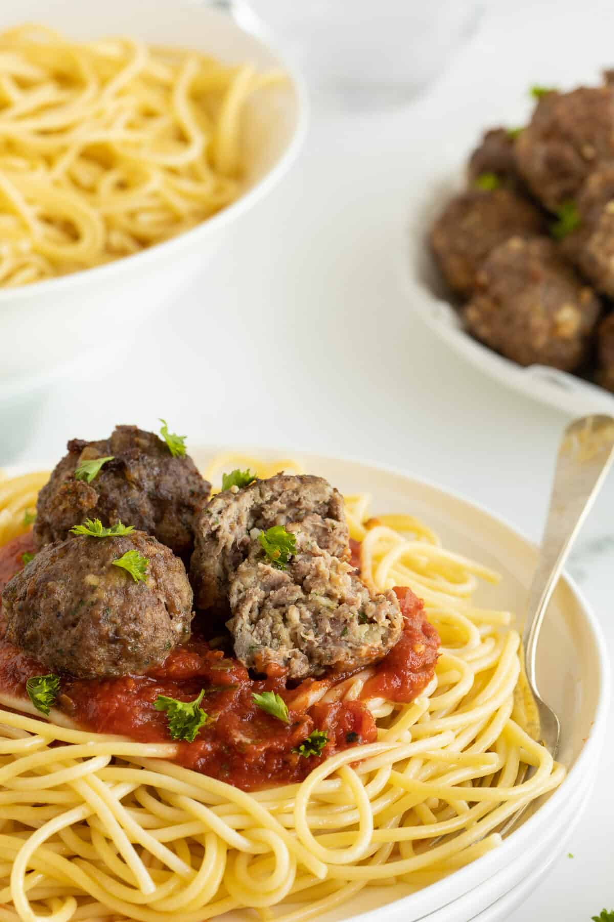 homemade meatballs on top of spaghetti and sauce on a white plate