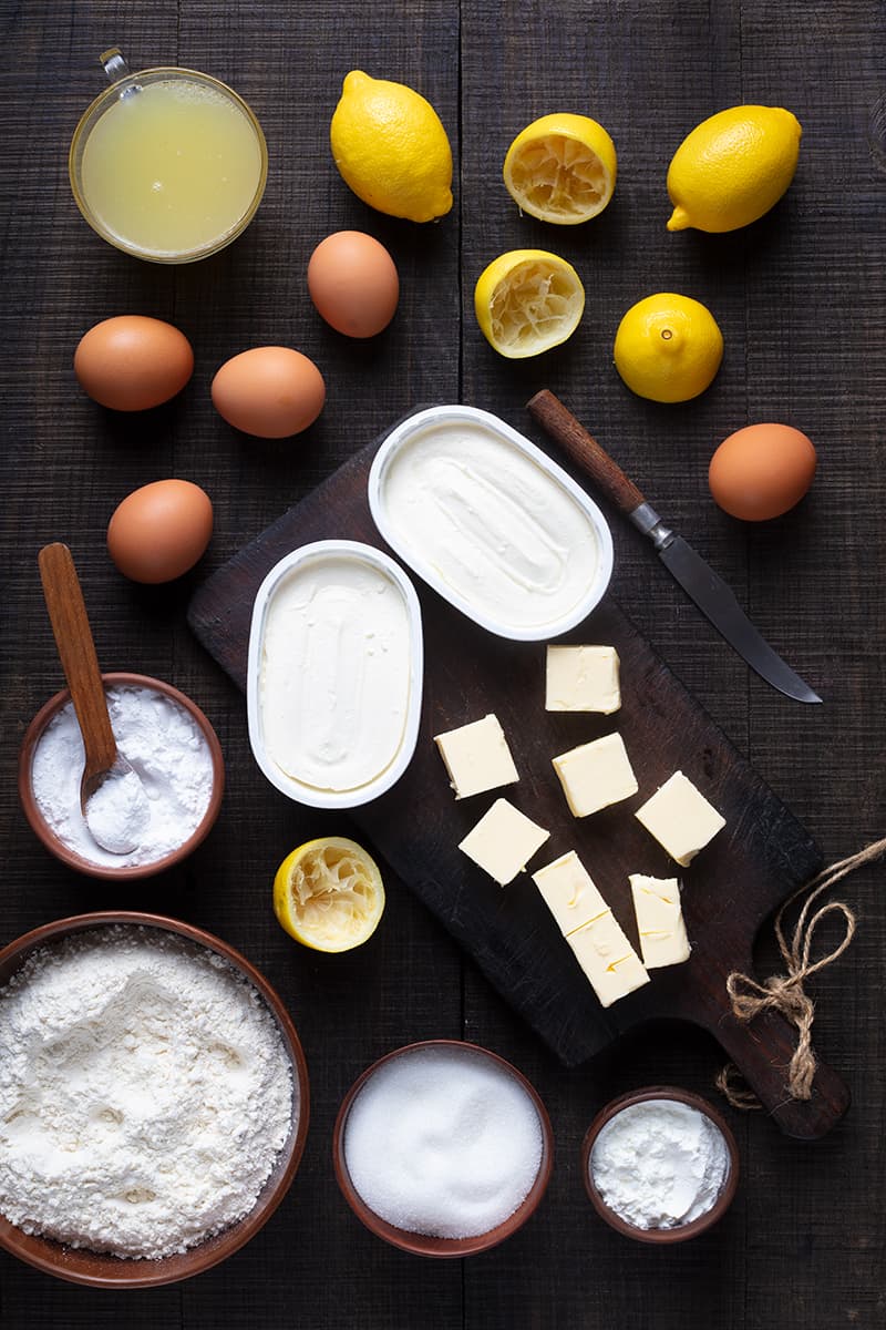 Lemon Cheesecake Bar ingredients on a dark wood background with wooden cutting board