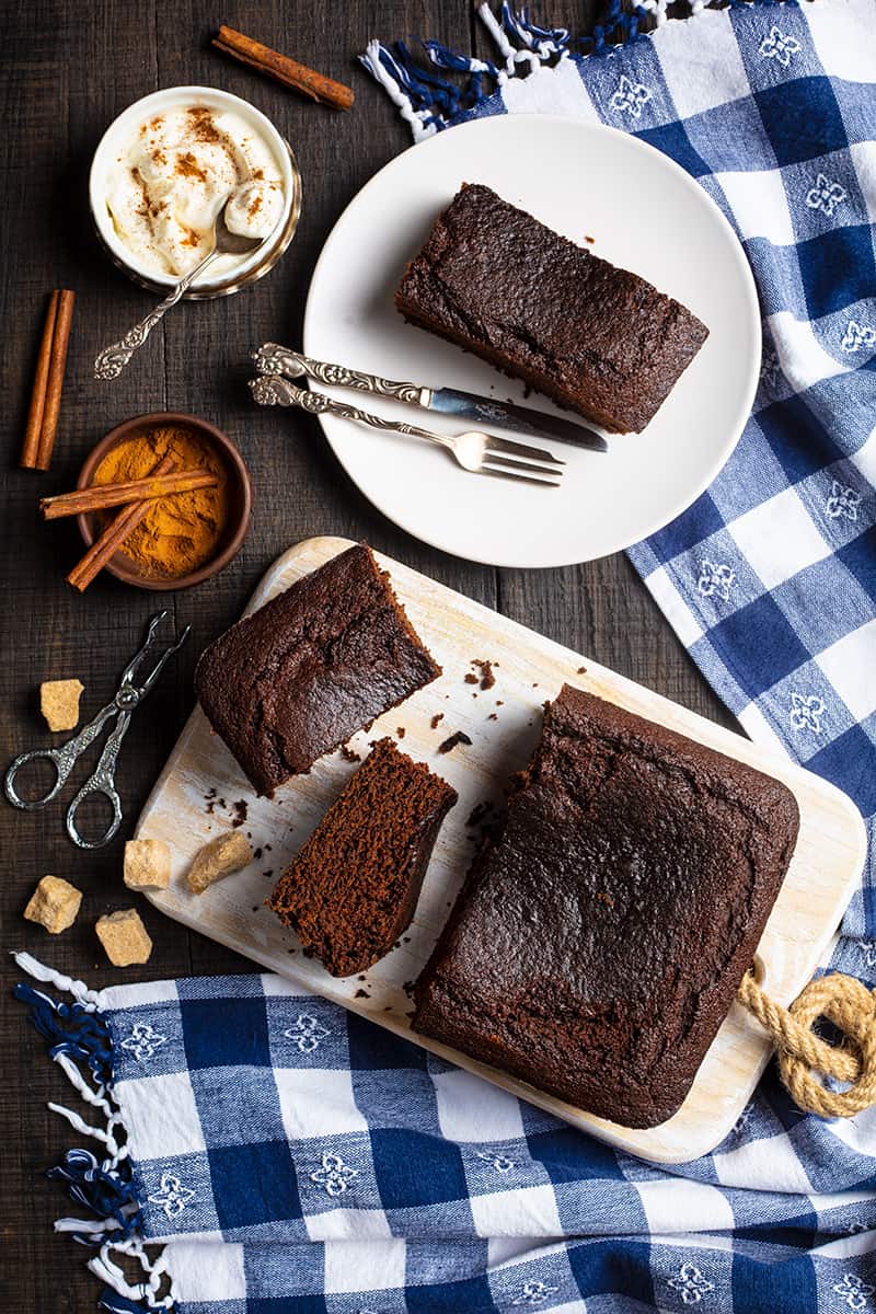 Old Fashioned Gingerbread slices on wooden cutting board and white plate with fork and bread knife