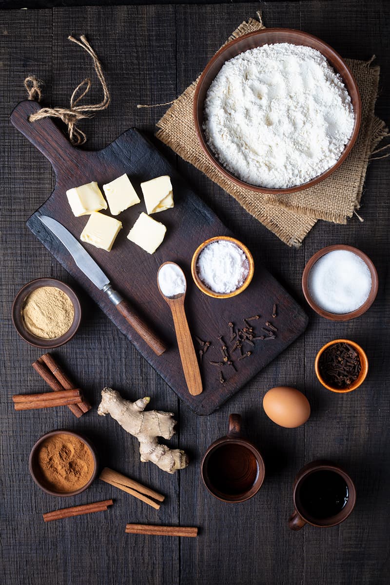 Old Fashioned Gingerbread ingredients in a wooden cutting board on a dark wood background