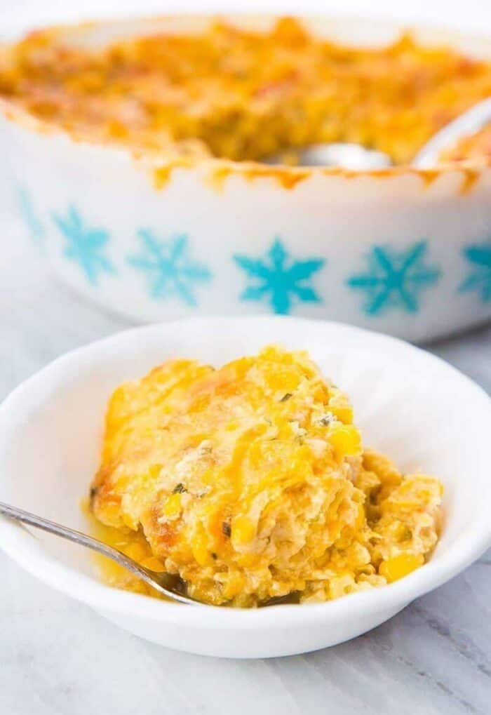 Creamy Scalloped Corn Casserole in a white serving bowl with a spoon