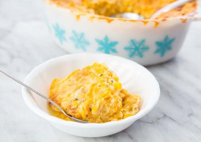 Creamy Scalloped Corn Casserole in a white serving bowl with a spoon