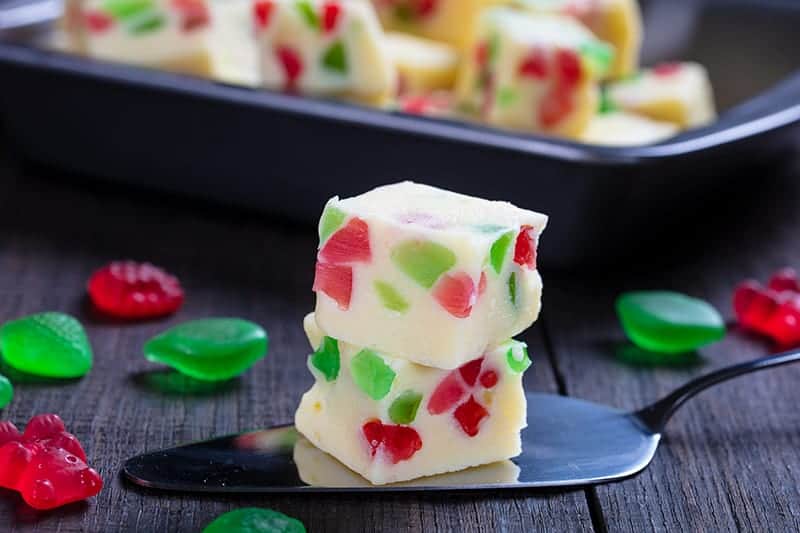 slice of Christmas Fudge in a cake spatula, jujubes scattered around and Christmas Fudge pan on its background