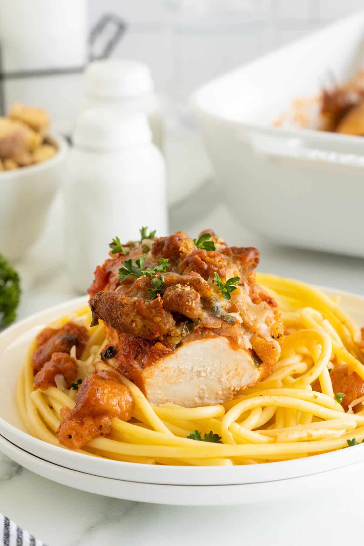 Chicken Parmesan Casserole on a white plate with pasta parsley on top