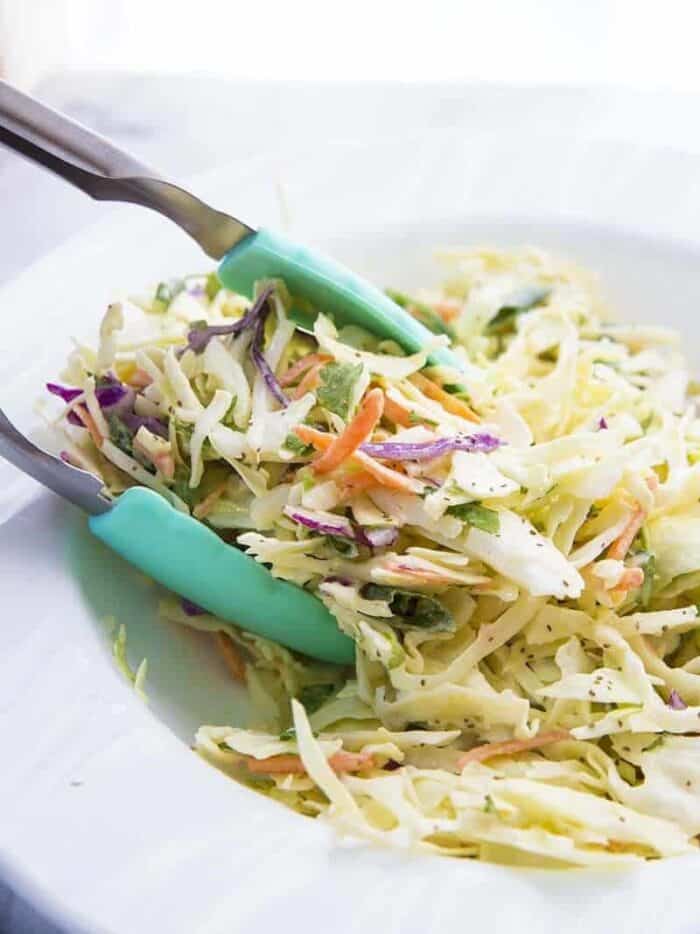 Dishing up homemade coleslaw with turquoise tongs