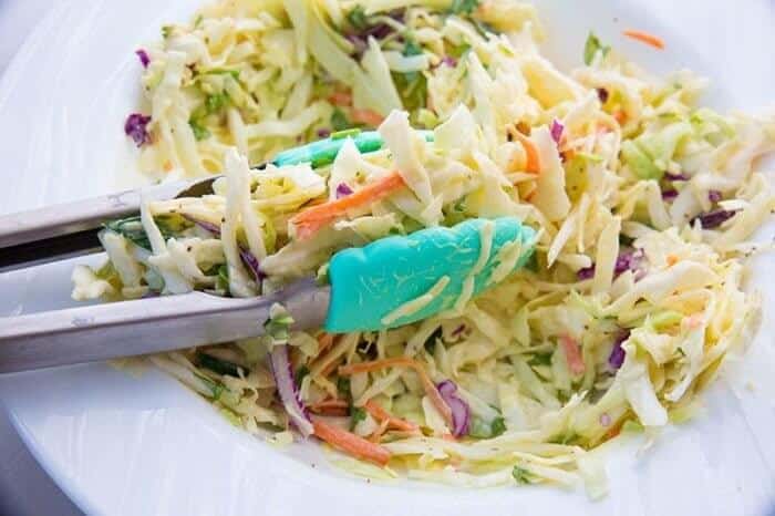 Kitchen tongs on Classic Homemade Coleslaw in a white plate