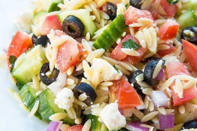 Greek Orzo Salad close up of tomatoes, orzo, black olives feta and purple onions in a white bowl