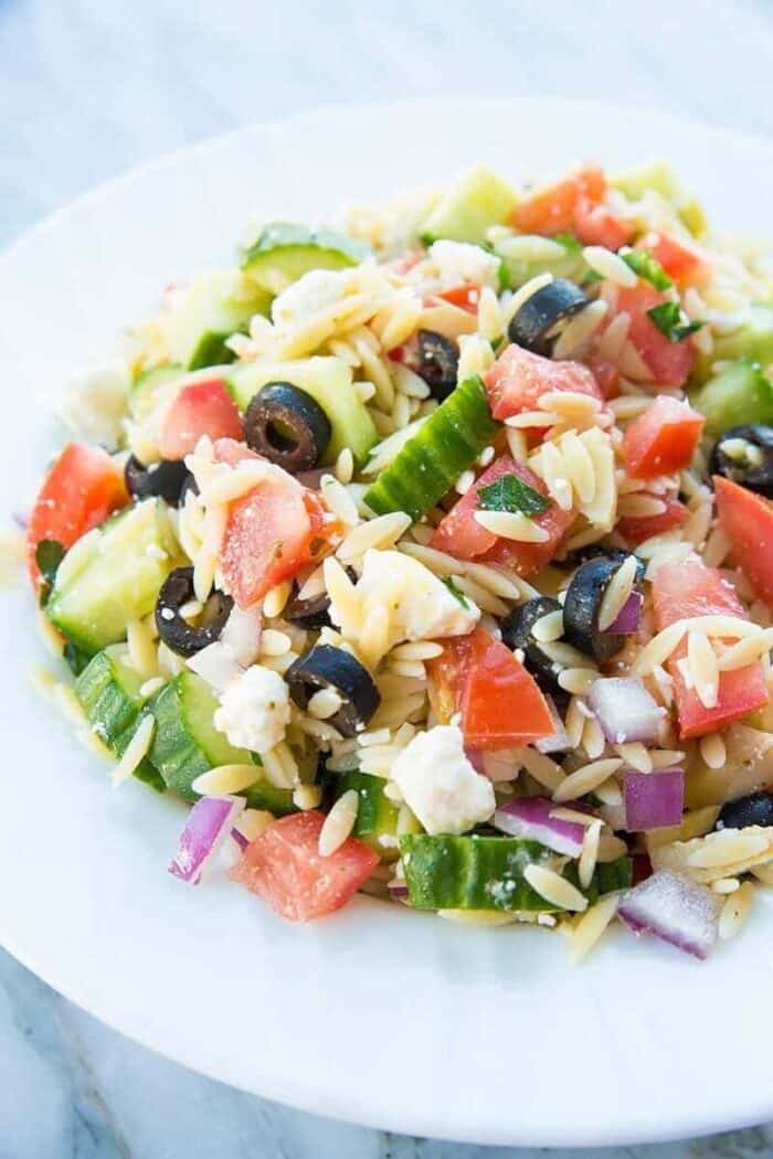 Greek Orzo Salad close up of tomatoes, orzo, black olives feta and purple onions in a white bowl