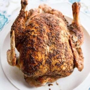 Close up of a whole roast chicken on a white plate