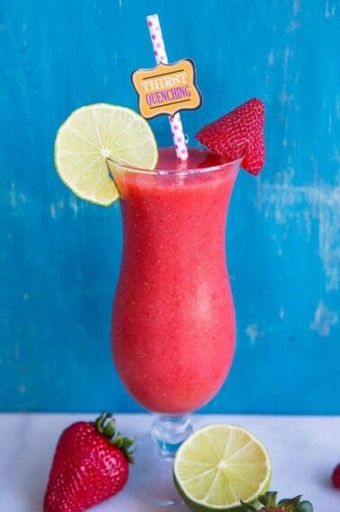 Close up of Hurricane style glass with Strawberry Daiquiri garnish with a slice of lime and fresh strawberries