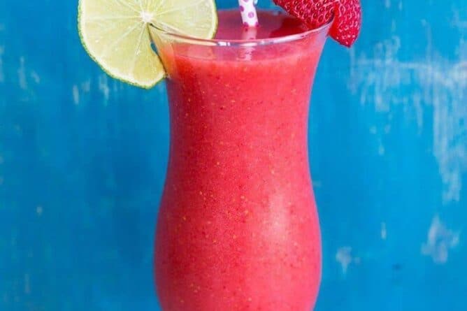 Close up of Hurricane style glass with Strawberry Daiquiri garnish with a slice of lime and fresh strawberries