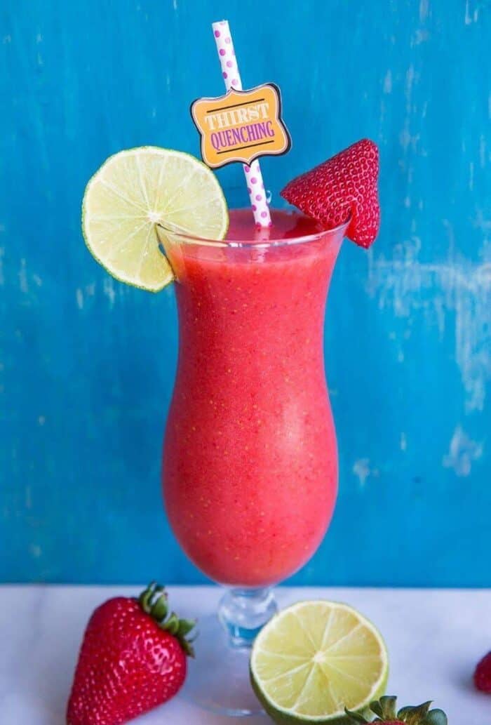 Close up of Hurricane style glass with Strawberry Daiquiri garnish with a slice of lime and fresh strawberries