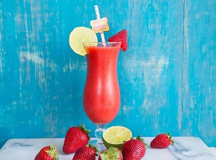 Strawberry Daiquiri in a hurricane style glass garnish with a slice of lime and fresh strawberries