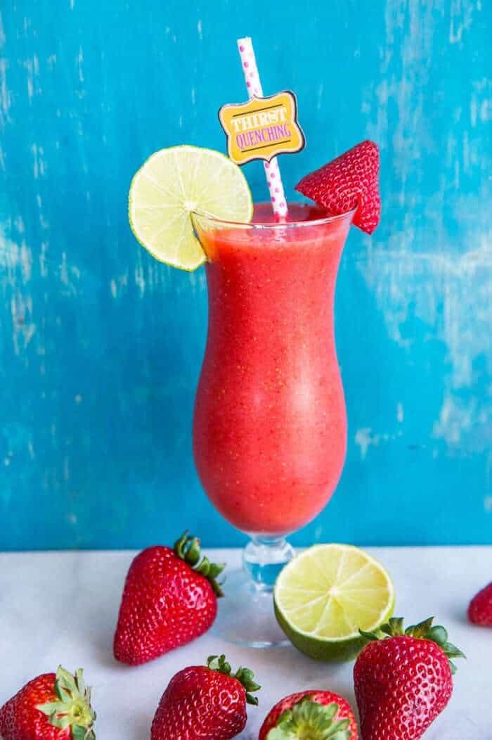 Close up of Hurricane style glass with Strawberry Daiquiri garnish with a slice of lime and fresh strawberries