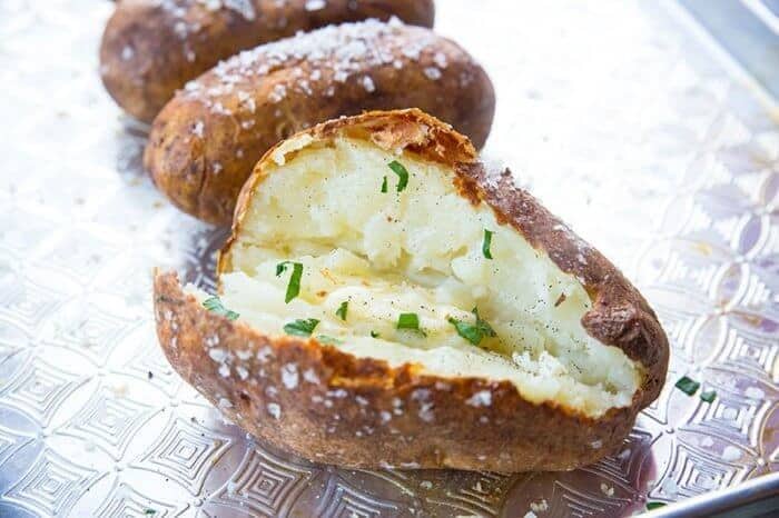 Potato split open with a salt covered skin on a baking sheet.